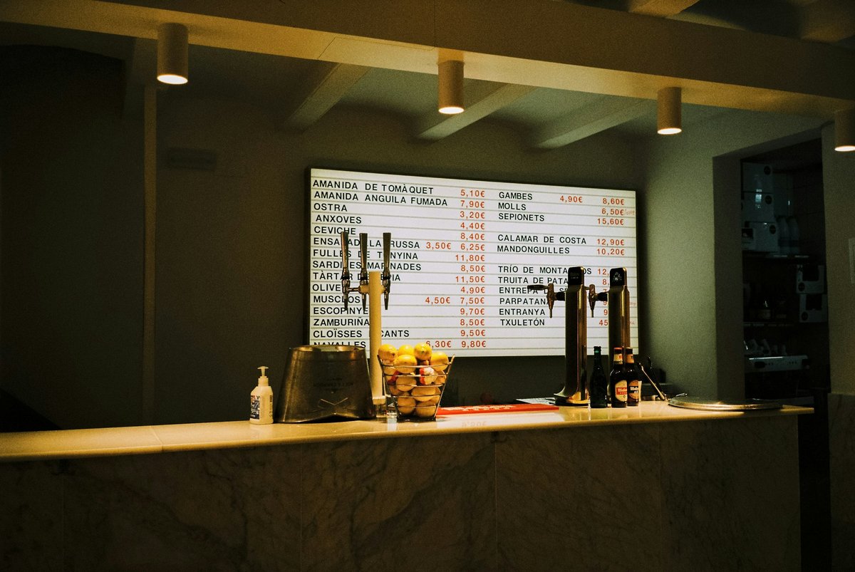 Barra de un bar con luz cálida y la pizarra de la carta al fondo.